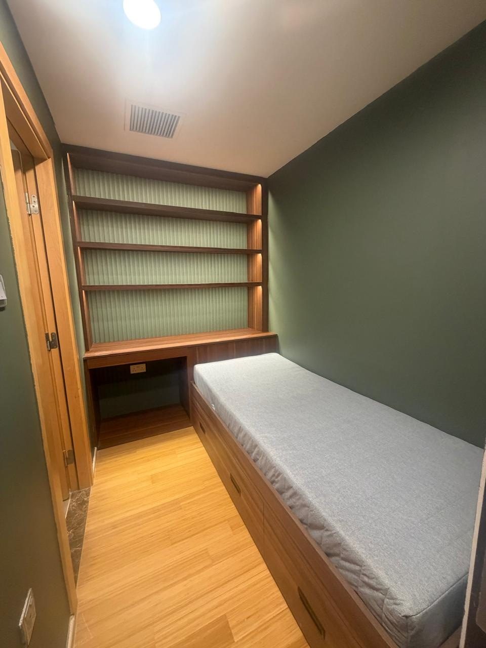 Green room with a built-in bed, lit wall shelves and a study nook in one warm finish