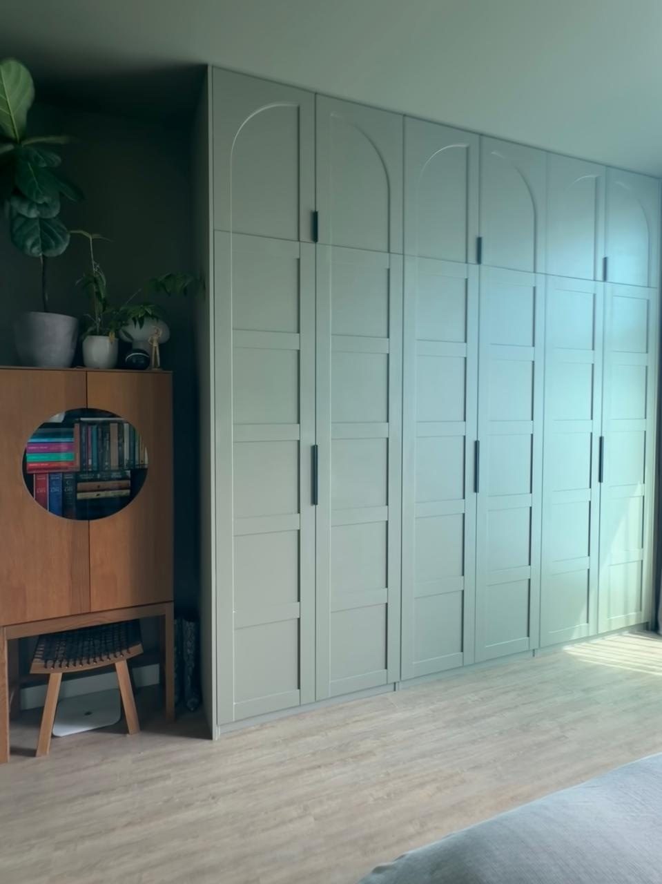Sage-green fitted wardrobe wall with arched upper doors and shaker-panelled lower doors