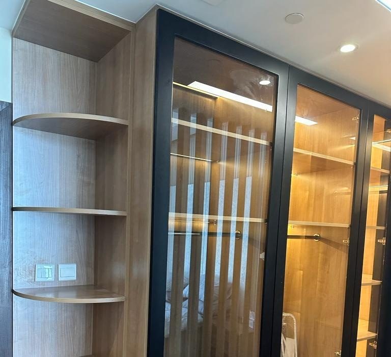 Curved open corner shelves beside black-framed glass wardrobe doors with lit interiors
