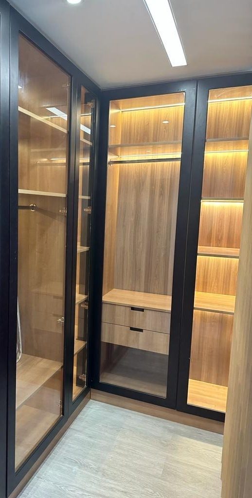 Walk-in closet with black-framed glass doors and warm, lit shelves